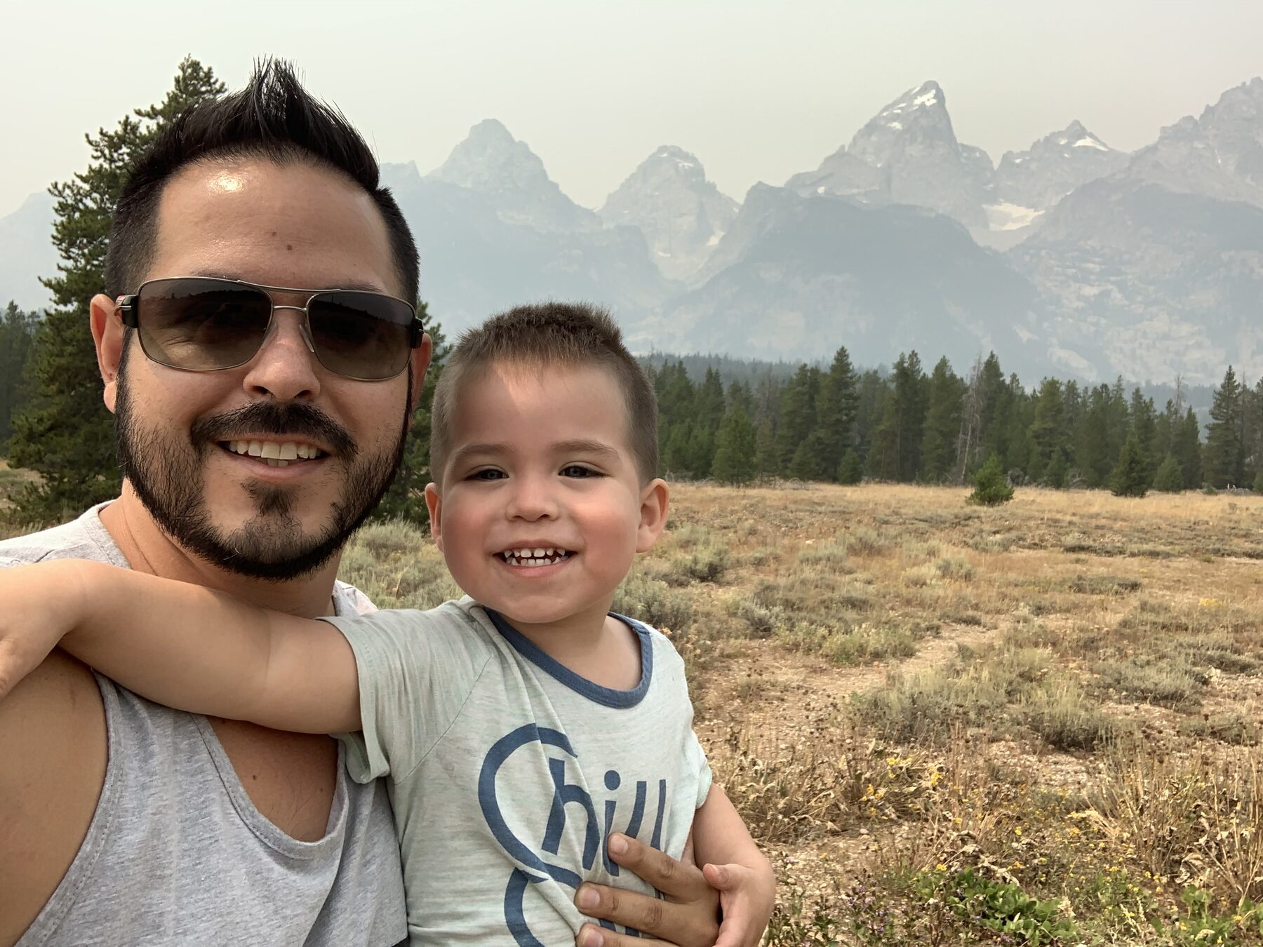 Young Oliver smiling with his dad in front of the mountains.