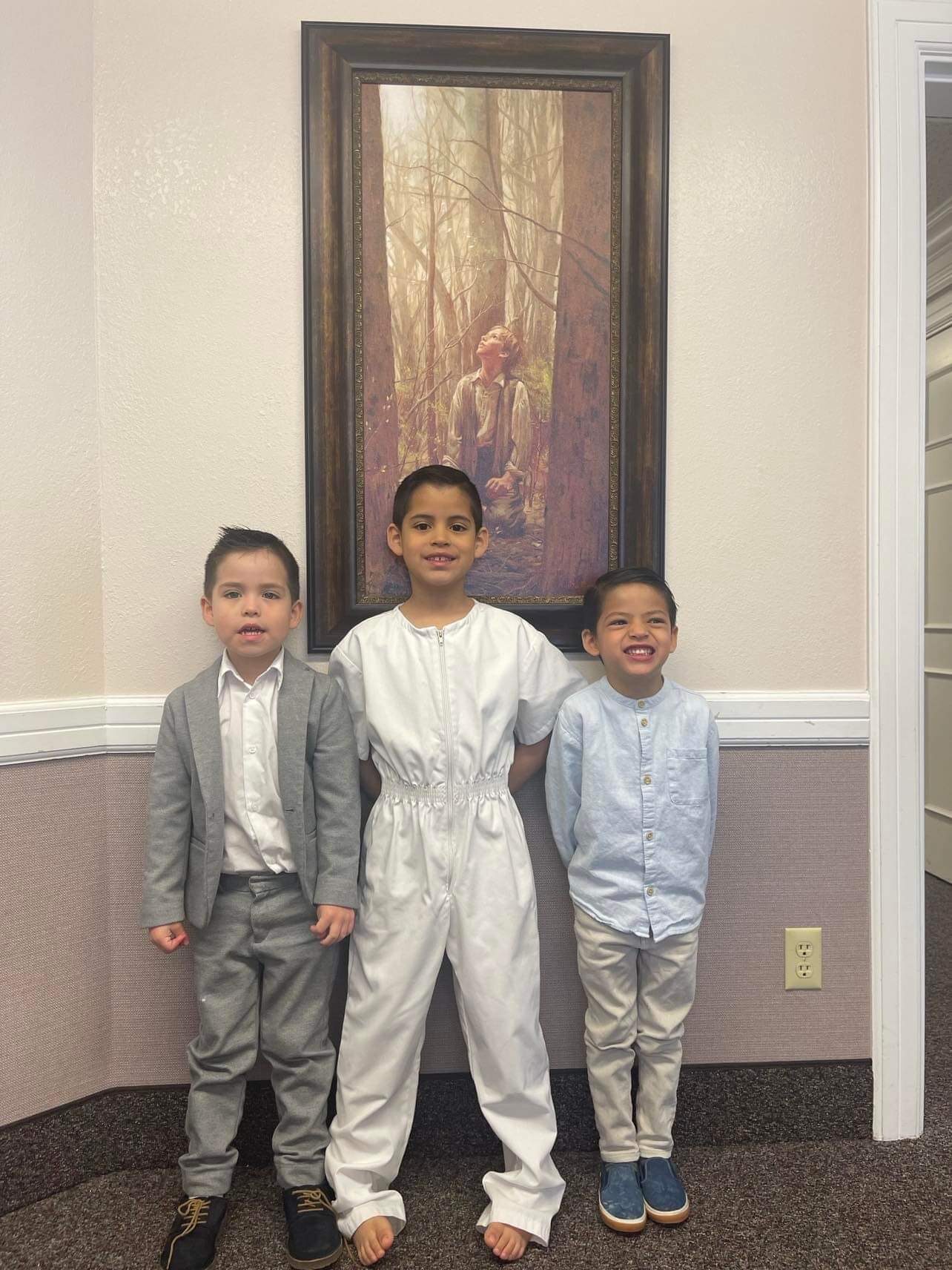Oliver in white baptismal clothing with his two brothers in front of a painting of Joseph Smith.