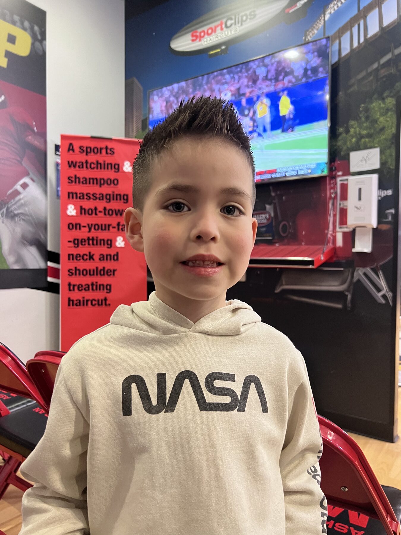 Oliver smiling after a fresh haircut in his NASA hoodie.