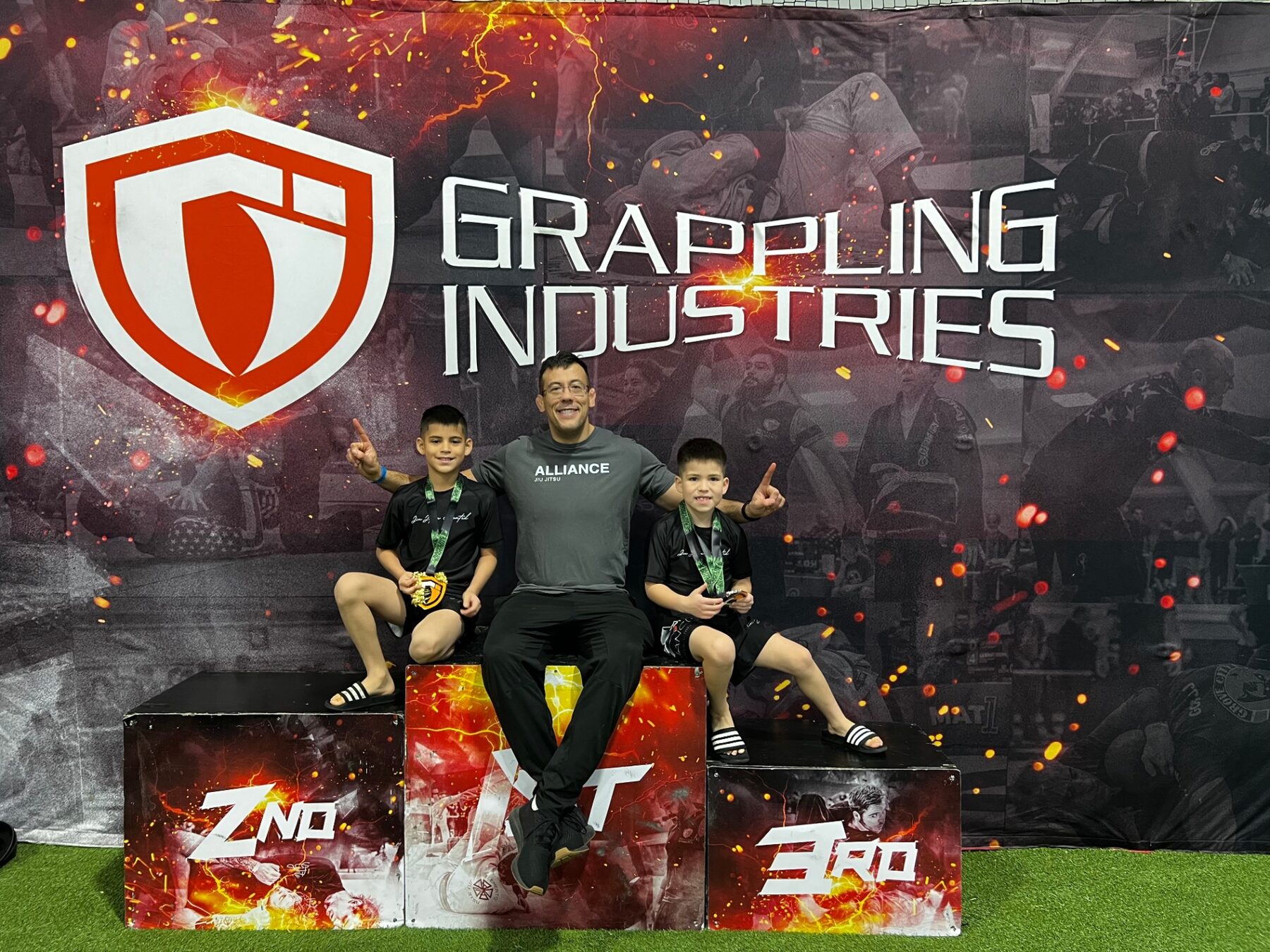 Oliver and his brother celebrating on the jiu-jitsu podium with their coach.